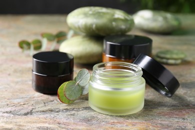 Jars of cream and eucalyptus leaves on textured table, closeup. Body care products