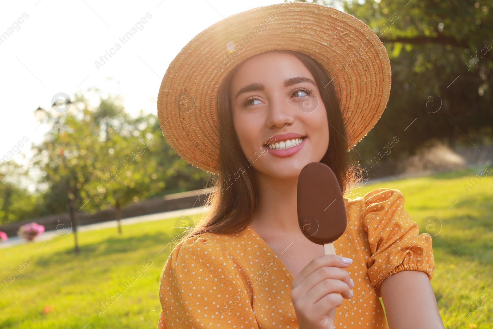 Photo of Beautiful young woman holding ice cream glazed in chocolate outdoors