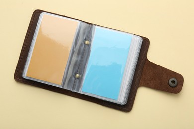 Photo of Leather business card holder with colorful cards on beige background, top view