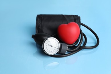 Photo of Blood pressure meter and toy heart on light blue background