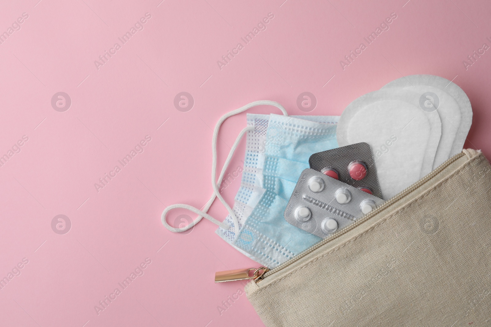 Photo of Bag with facial mask, pills and sanitary pads on pink background, top view. Space for text