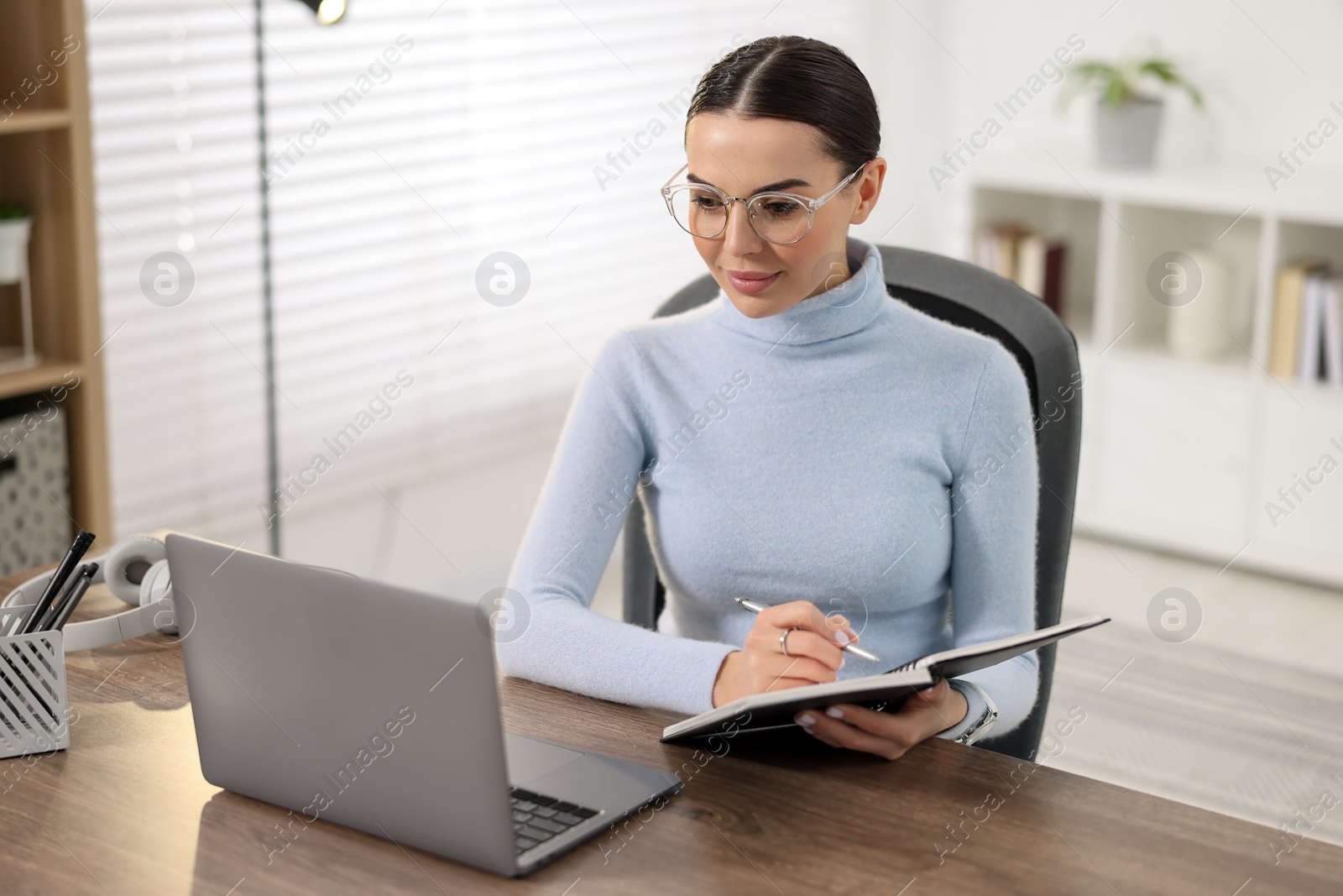 Photo of Young woman in glasses watching webinar at table in office