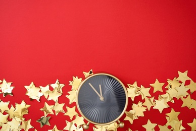 Photo of Alarm clock and golden confetti on red background, flat lay with space for text. New Year countdown