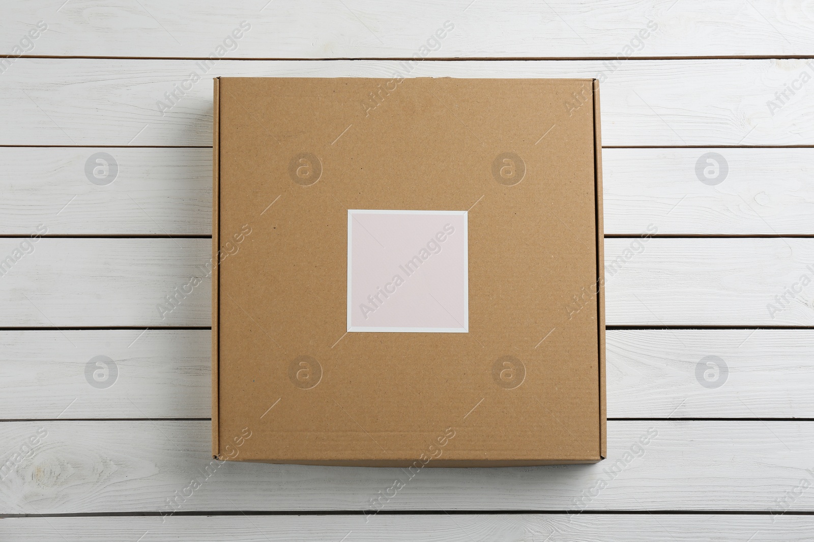 Photo of Cardboard box on white wooden background, top view