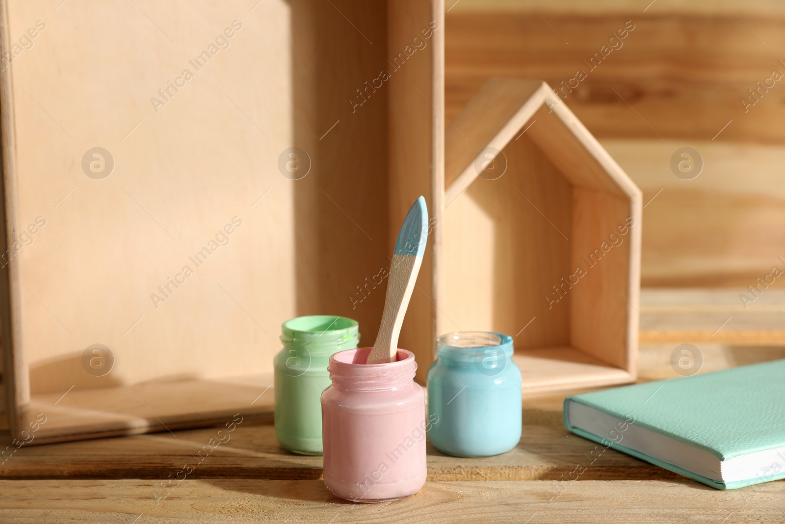 Photo of Jars of paints with brush on wooden table. Interior elements