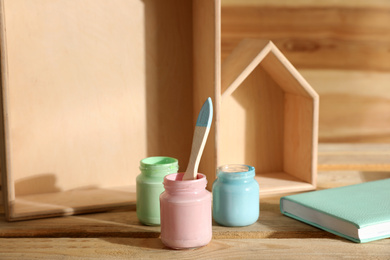 Photo of Jars of paints with brush on wooden table. Interior elements