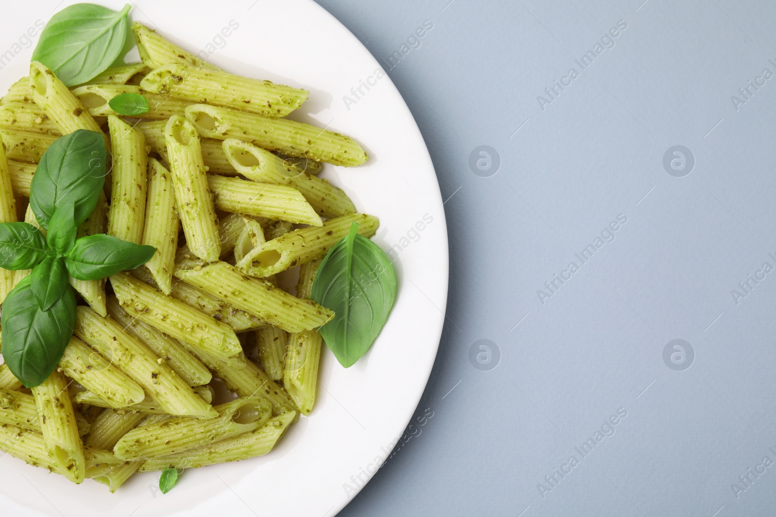 Photo of Delicious pasta with pesto sauce and basil on light grey background, top view. Space for text