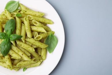 Photo of Delicious pasta with pesto sauce and basil on light grey background, top view. Space for text