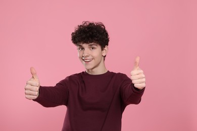 Photo of Portrait of smiling teenage boy showing thumbs up on pink background