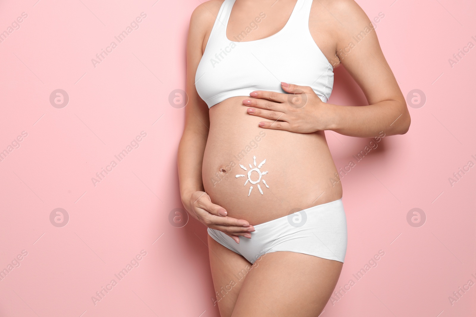 Photo of Sun painted with body cream on pregnant woman's belly against color background, closeup