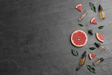 Flat lay composition with grapefruit slices and bottles of essential oil on grey background, space for text