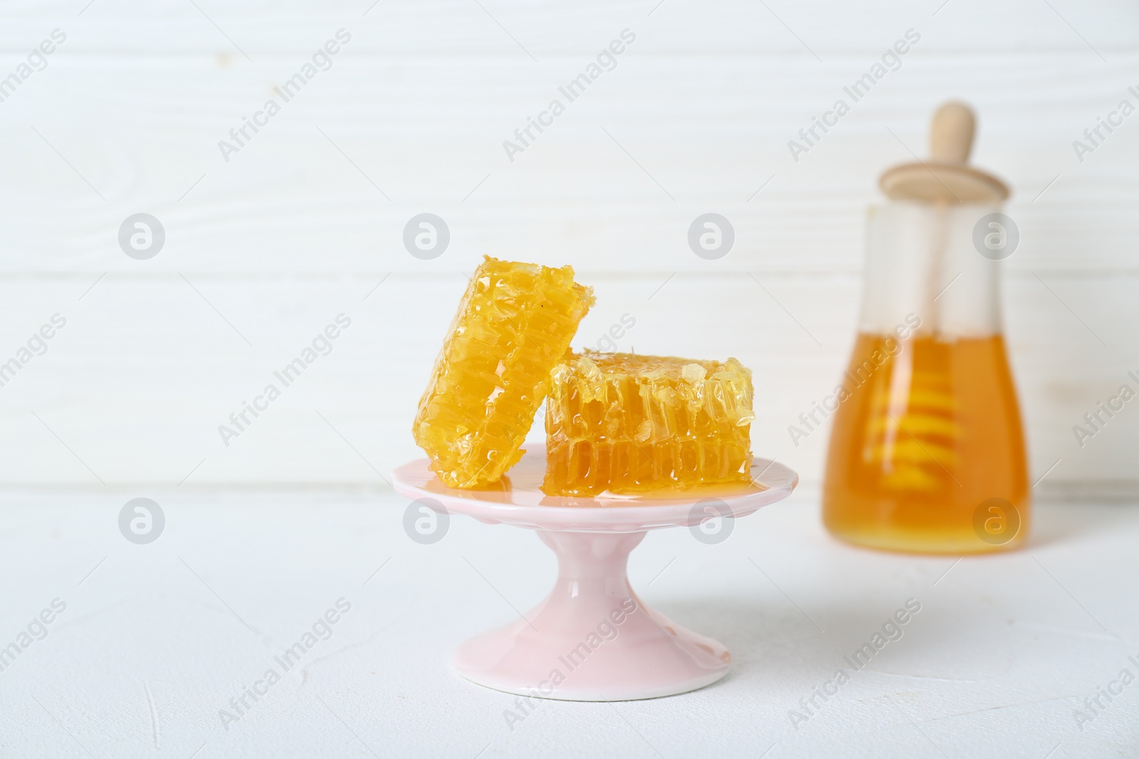 Photo of Stand with natural honeycombs and honey on white table, selective focus. Space for text