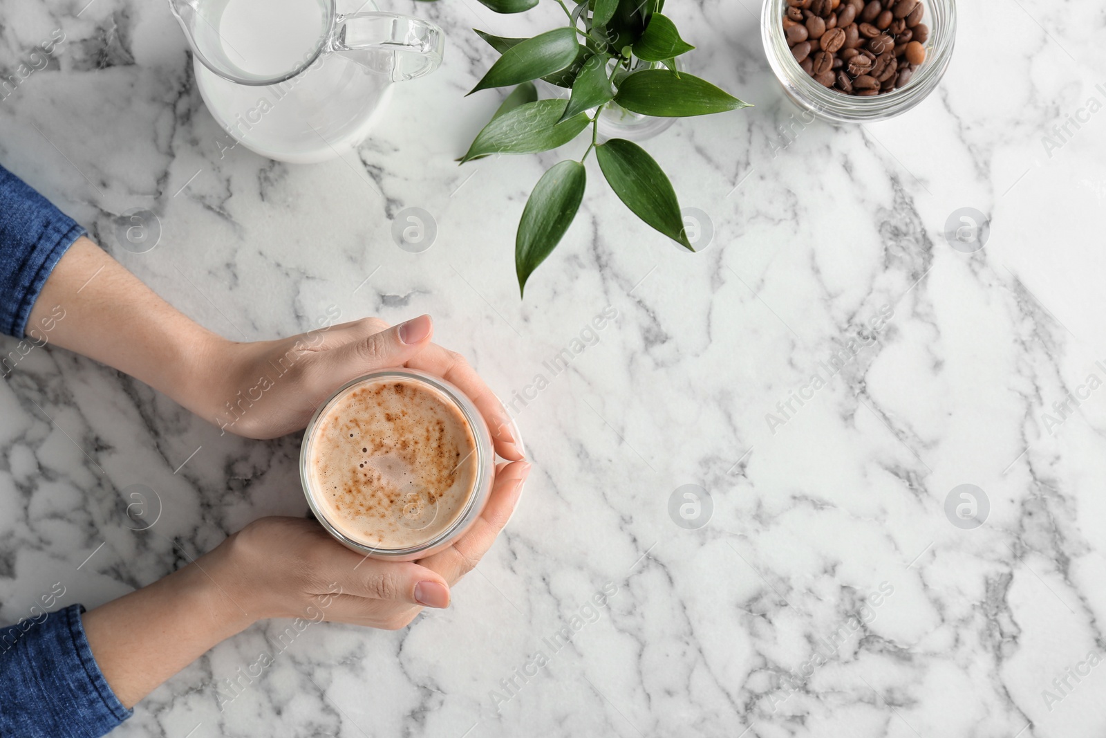 Photo of Woman with glass of aromatic hot coffee at marble table, top view