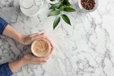 Photo of Woman with glass of aromatic hot coffee at marble table, top view