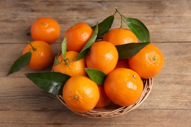 Photo of Delicious tangerines with leaves on wooden table, above view