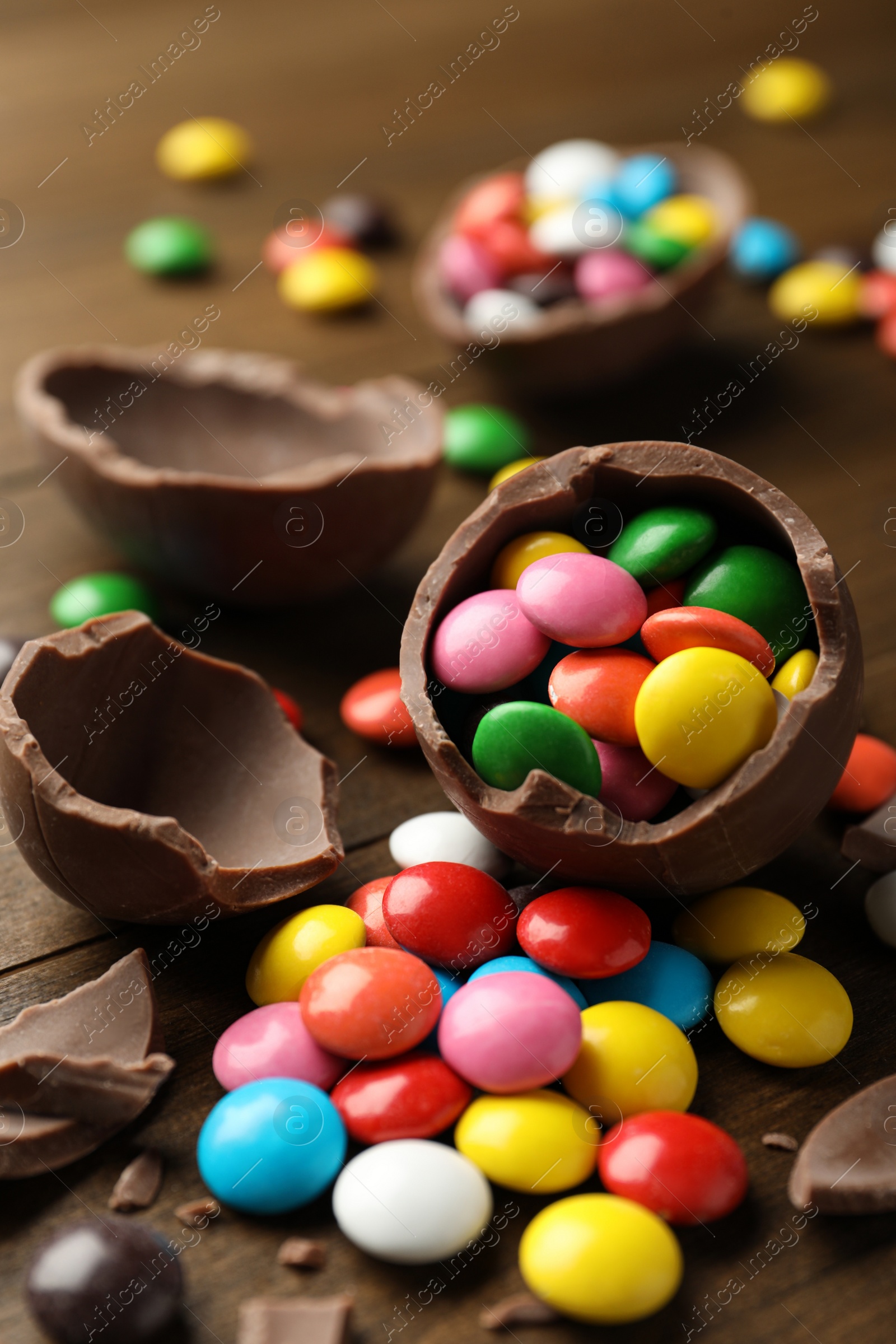 Photo of Broken chocolate eggs and colorful candies on wooden table, closeup