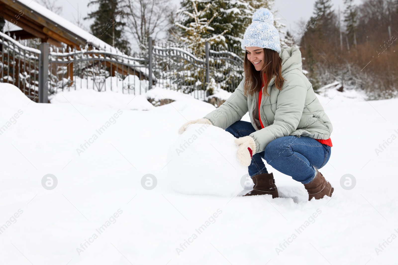 Photo of Happy woman making ball for snowman outdoors. Winter vacation