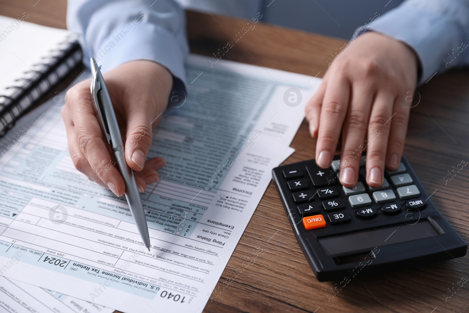 Photo of Payroll. Woman using calculator while working with tax return forms at wooden table, closeup