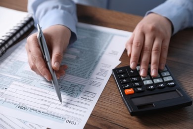 Payroll. Woman using calculator while working with tax return forms at wooden table, closeup