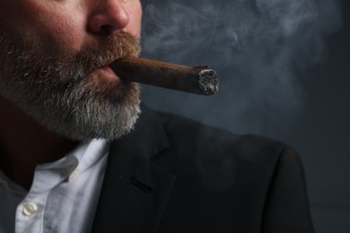 Photo of Bearded man smoking cigar against dark grey background, closeup