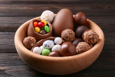 Photo of Tasty chocolate eggs and sweets in bowl on wooden table