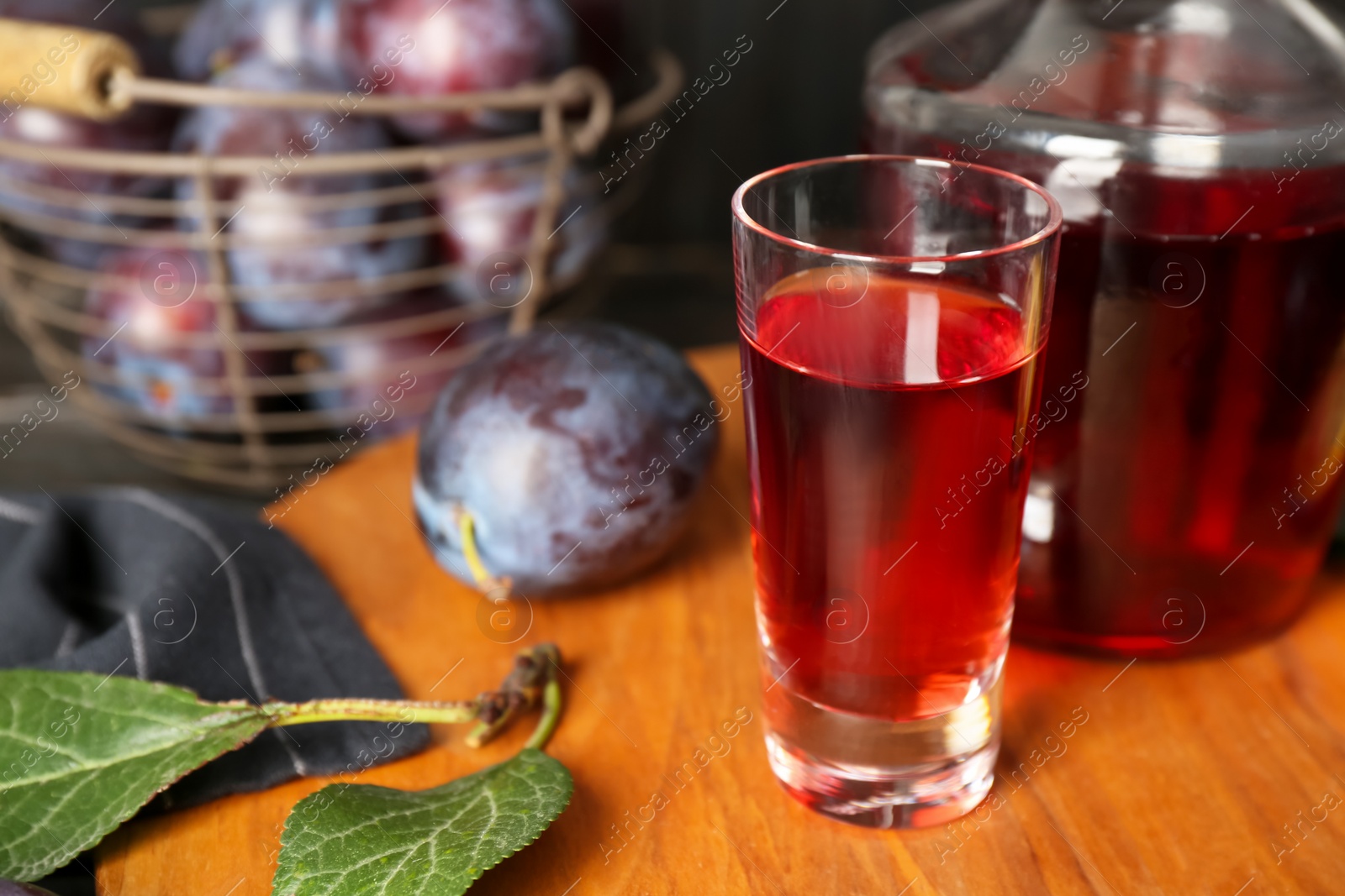 Photo of Delicious plum liquor in shot glass on wooden board. Homemade strong alcoholic beverage