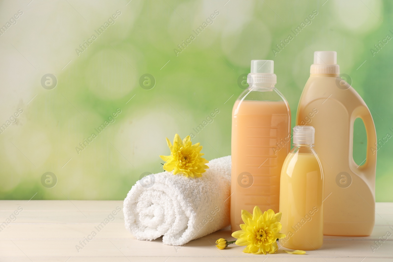 Photo of Bottles of laundry detergents, towel and beautiful flowers on white wooden table. Space for text