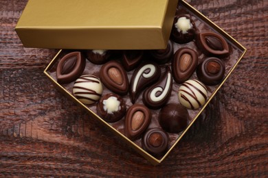 Open box of delicious chocolate candies on wooden table, top view