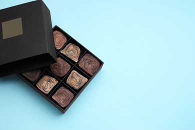 Photo of Box of tasty chocolate candies on light blue background, top view. Space for text