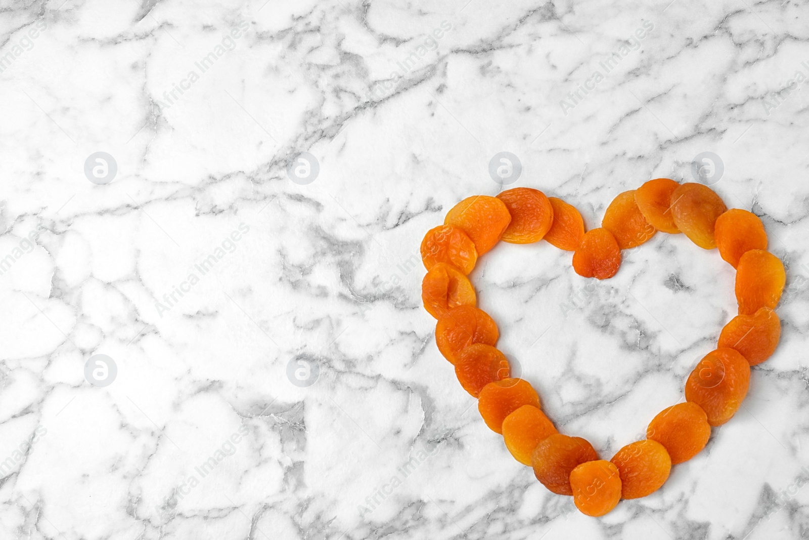 Photo of Heart made of apricots on marble background, top view with space for text. Dried fruit as healthy food