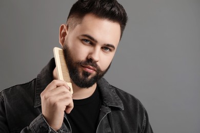 Handsome young man combing beard on grey background. Space for text