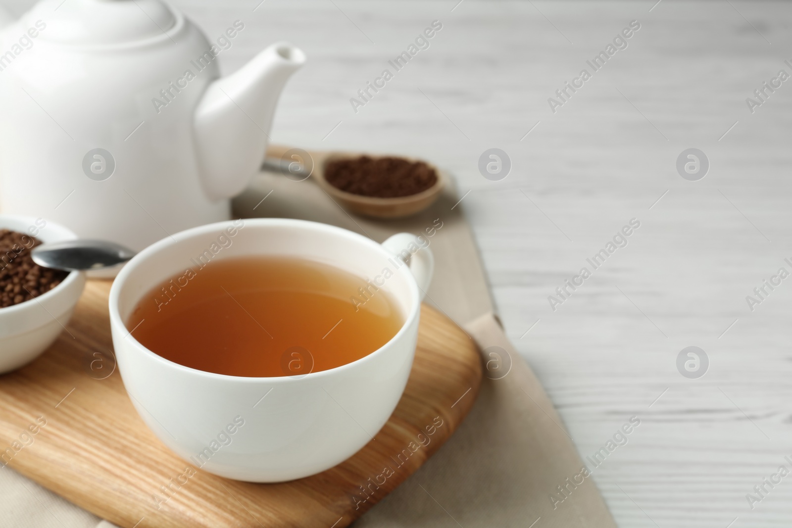 Photo of Cup of buckwheat tea on white wooden table. Space for text