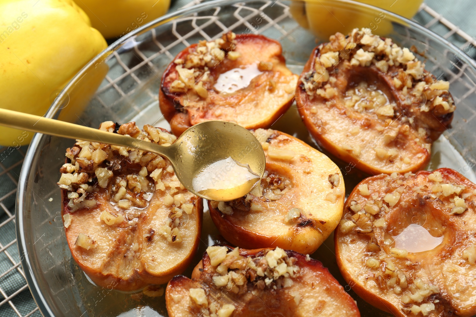 Photo of Pouring tasty honey onto baked quinces in bowl on table, closeup