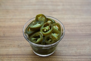 Photo of Glass bowl of pickled green jalapeno peppers on wooden table, closeup