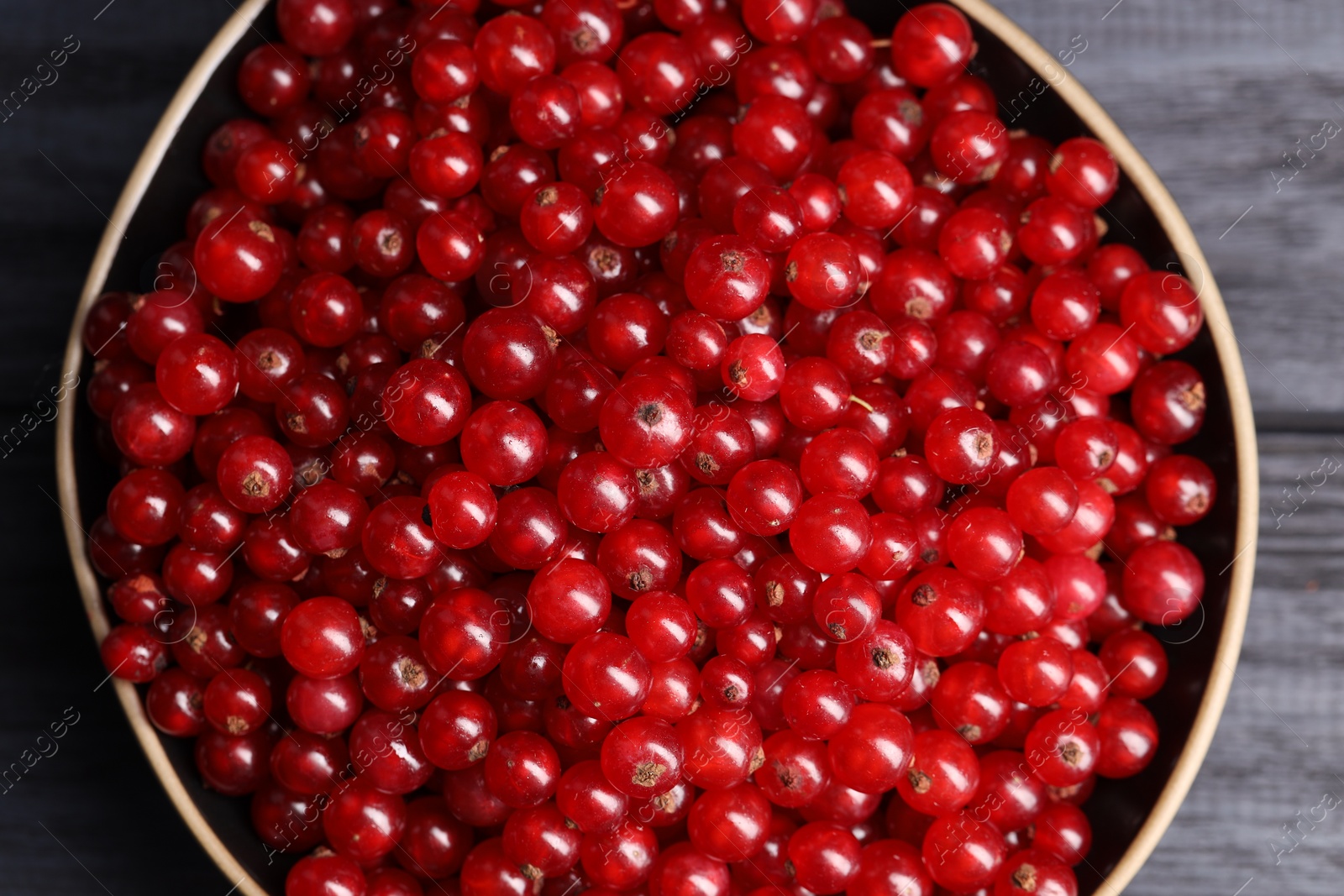 Photo of Ripe red currants in bowl on wooden rustic table, top view