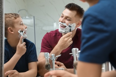 Photo of Dad shaving and son imitating him at mirror in bathroom