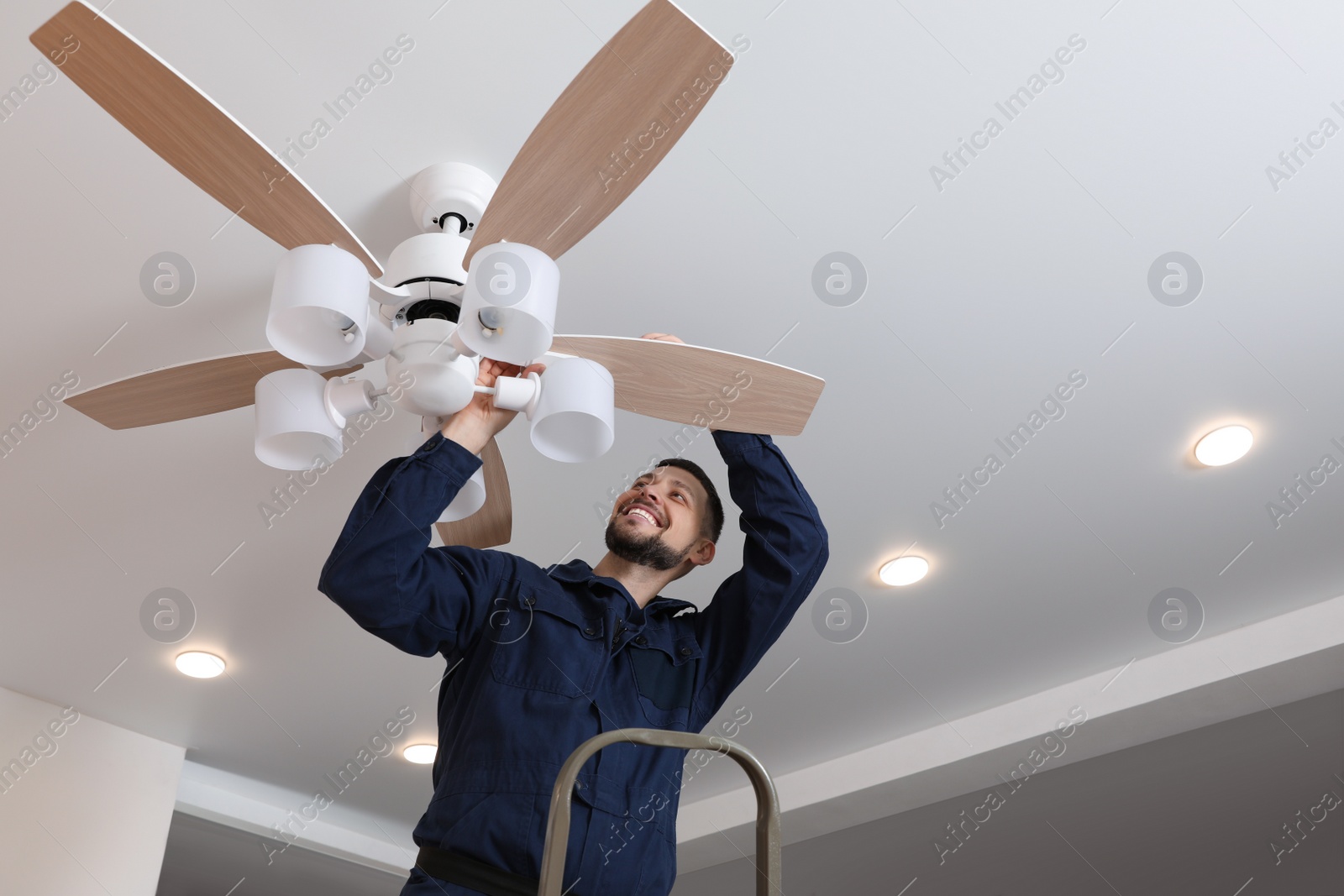 Photo of Electrician repairing ceiling fan with lamps indoors