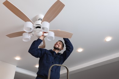 Photo of Electrician repairing ceiling fan with lamps indoors