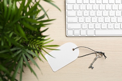 Photo of Key with blank tag and computer keyboard on wooden table, top view. Keyword concept