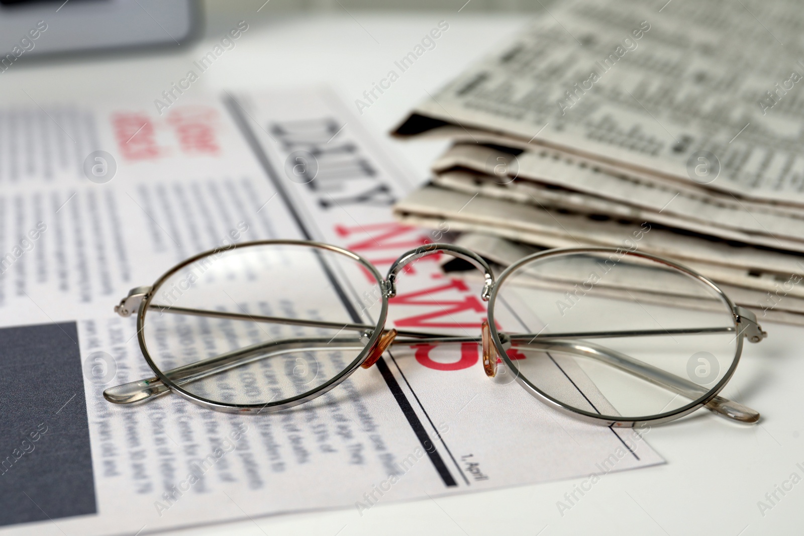 Photo of Stack of newspapers and glasses on white table, closeup