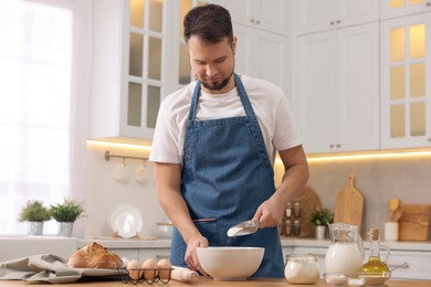 Making bread. Man putting flour into bowl at wooden table in kitchen