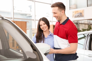 Photo of Young couple near auto in salon. Buying new car