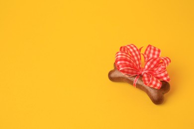 Photo of Bone shaped dog cookie with red bow on yellow background, above view. Space for text