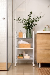 Photo of Vase with green branches and different toiletries on rack in bathroom