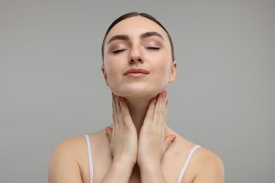 Beautiful woman touching her neck on grey background