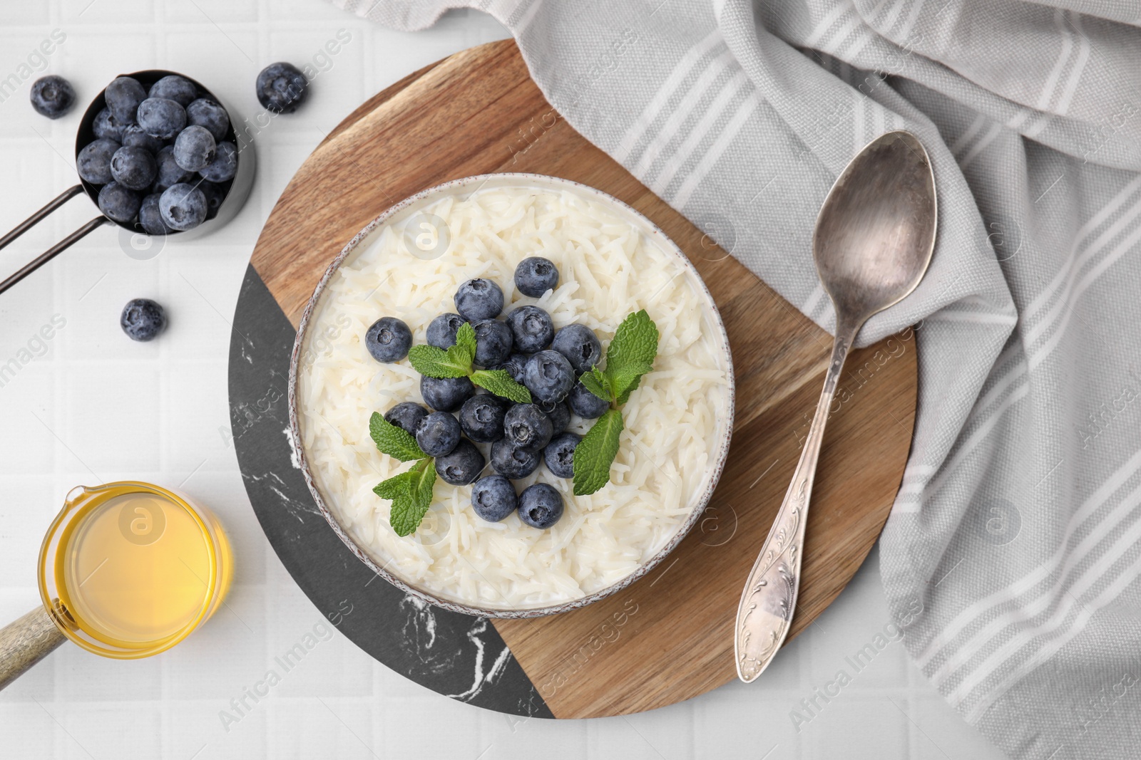 Photo of Bowl of delicious rice porridge with blueberries and mint served on table, flat lay