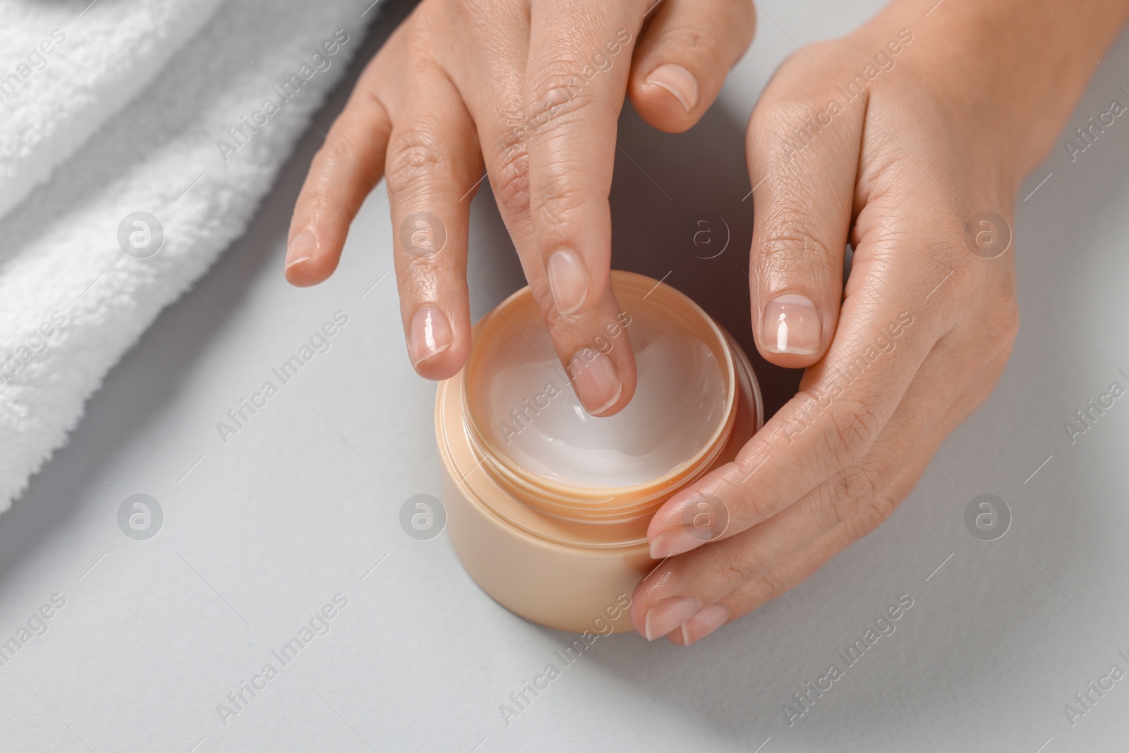 Photo of Woman with jar of hand cream and towel on light grey background, closeup