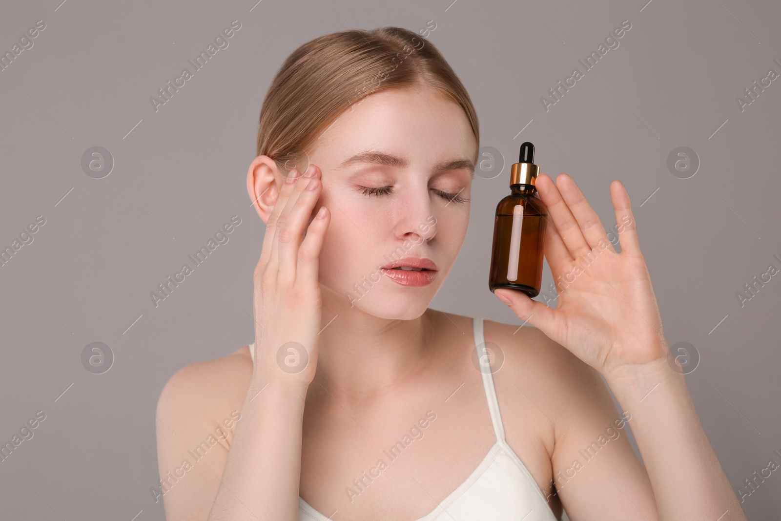 Photo of Beautiful young woman with bottle of essential oil on light grey background