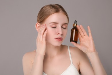 Beautiful young woman with bottle of essential oil on light grey background