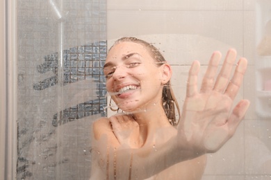 Photo of Young woman taking shower, view through glass door